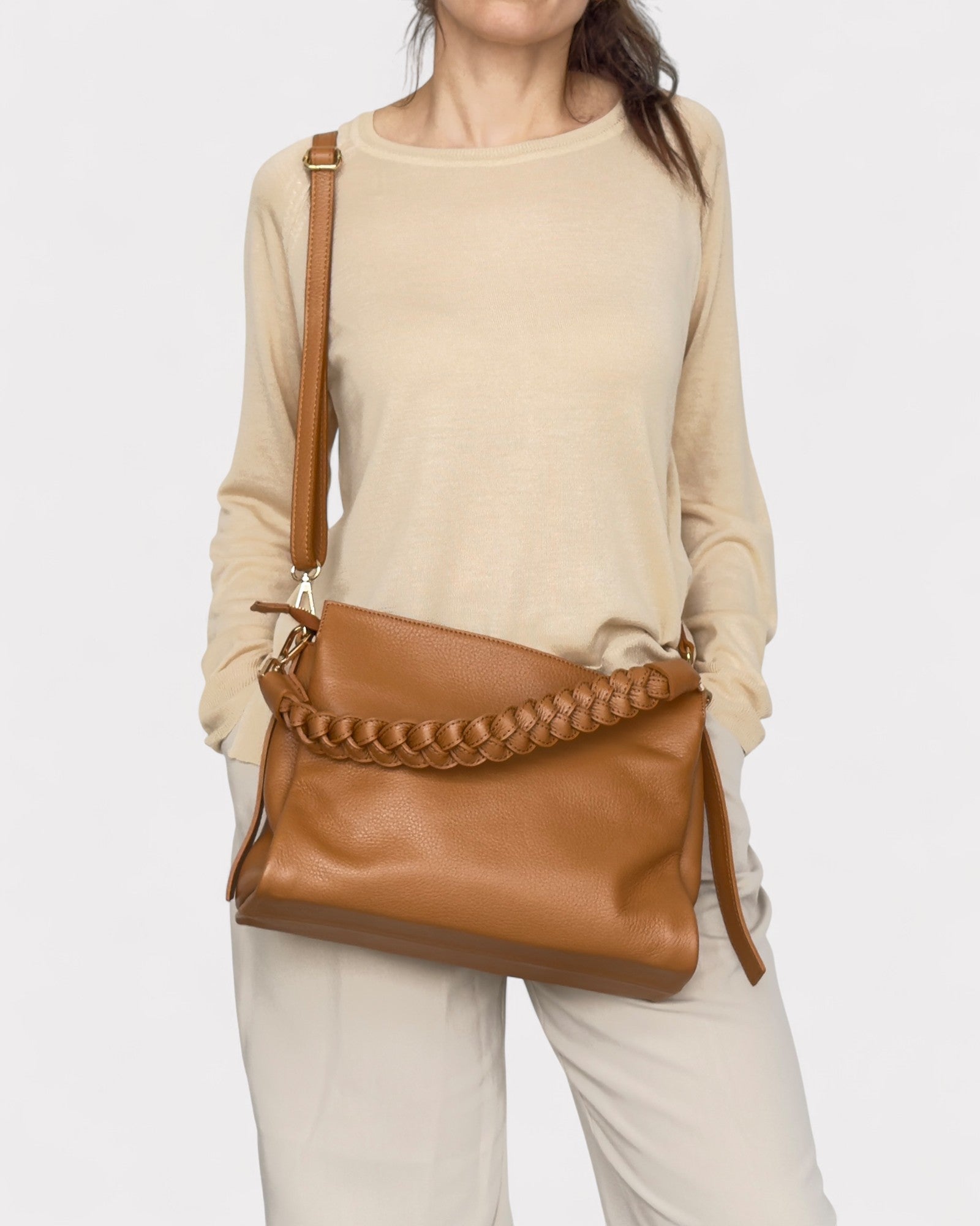 Person wearing a beige sweater and holding a Tan leather handbag with braided detail on a white background