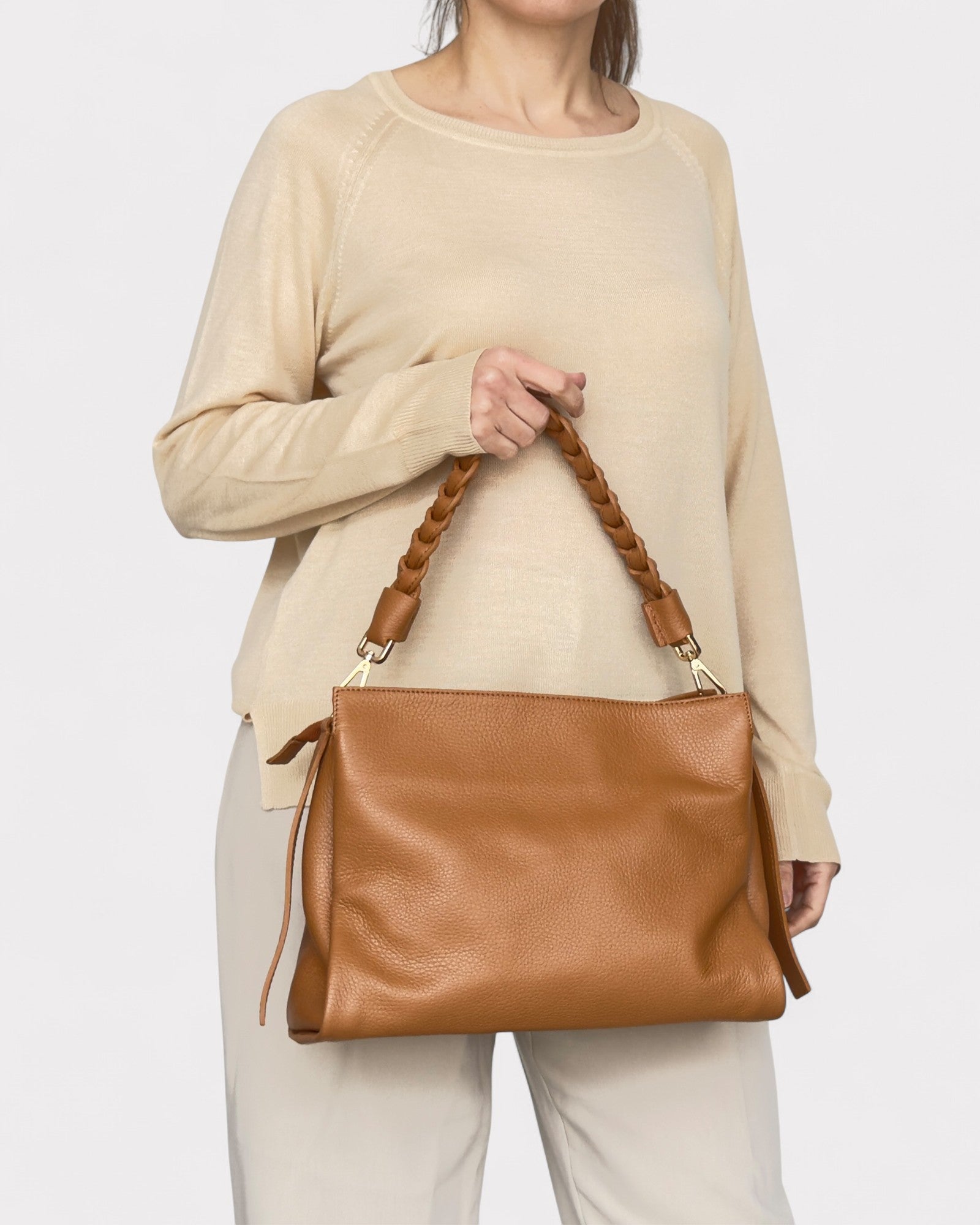 Person holding a Tan leather handbag with braided handle on a white background