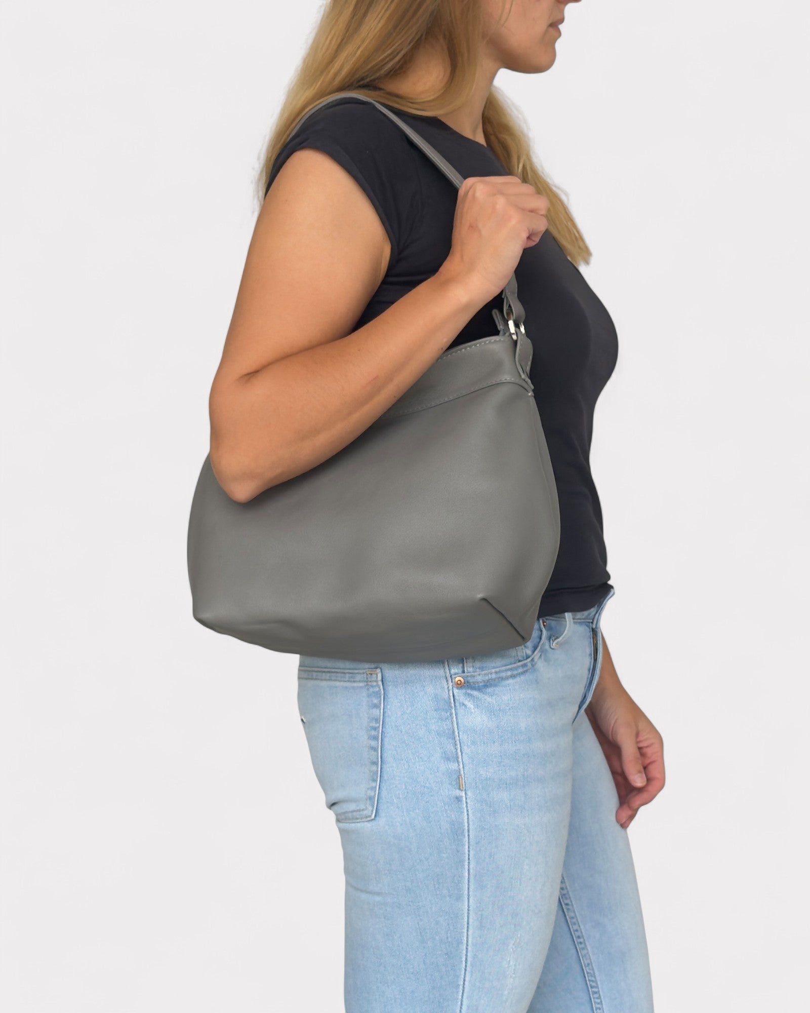Woman carrying a gray shoulder bag on a plain background