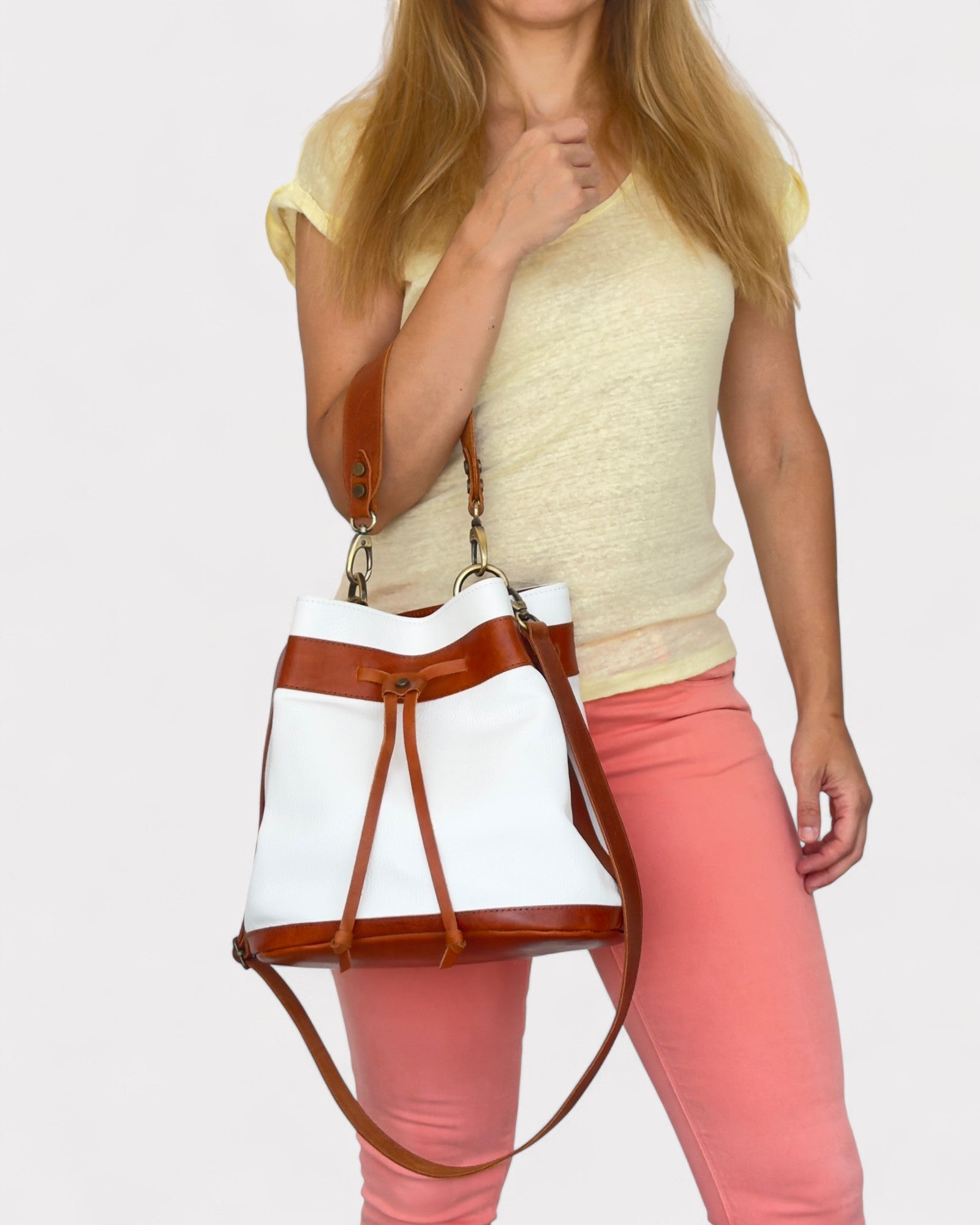 Woman holding a white bucket bag with brown leather straps against a plain background