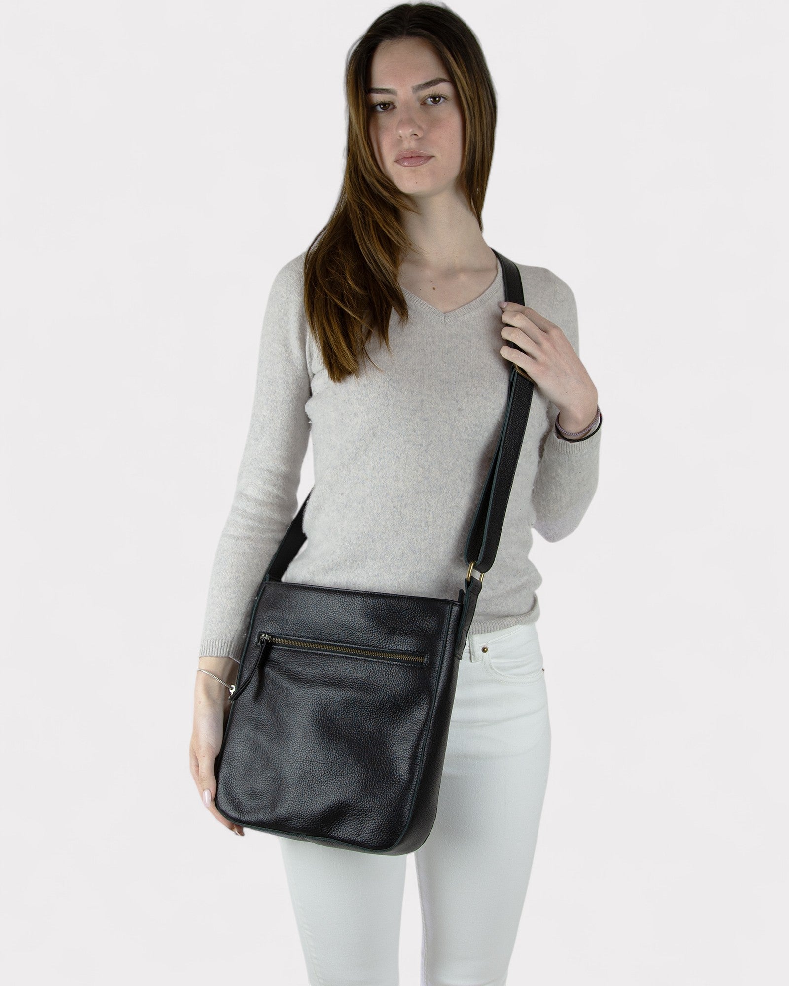 Woman holding a black leather crossbody bag against a white background