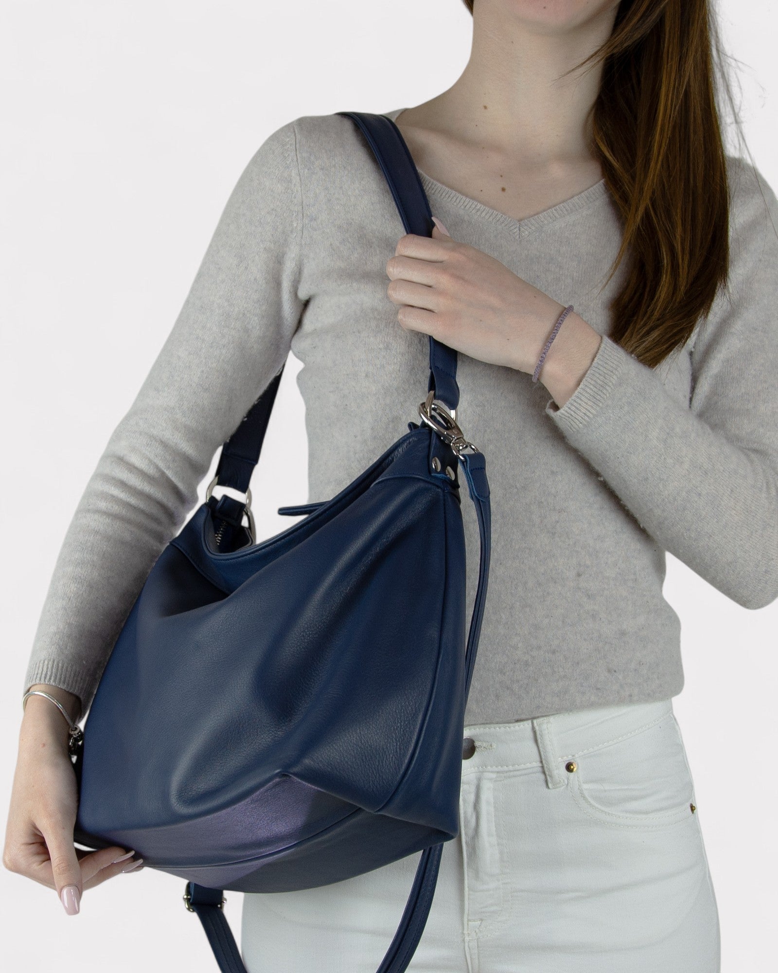 Person wearing a gray sweater and white pants with a navy blue handbag on a light gray background