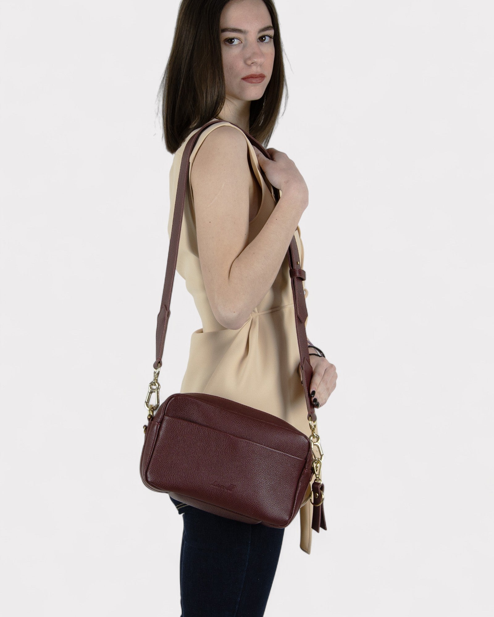 Woman holding a burgundy leather handbag against a plain background