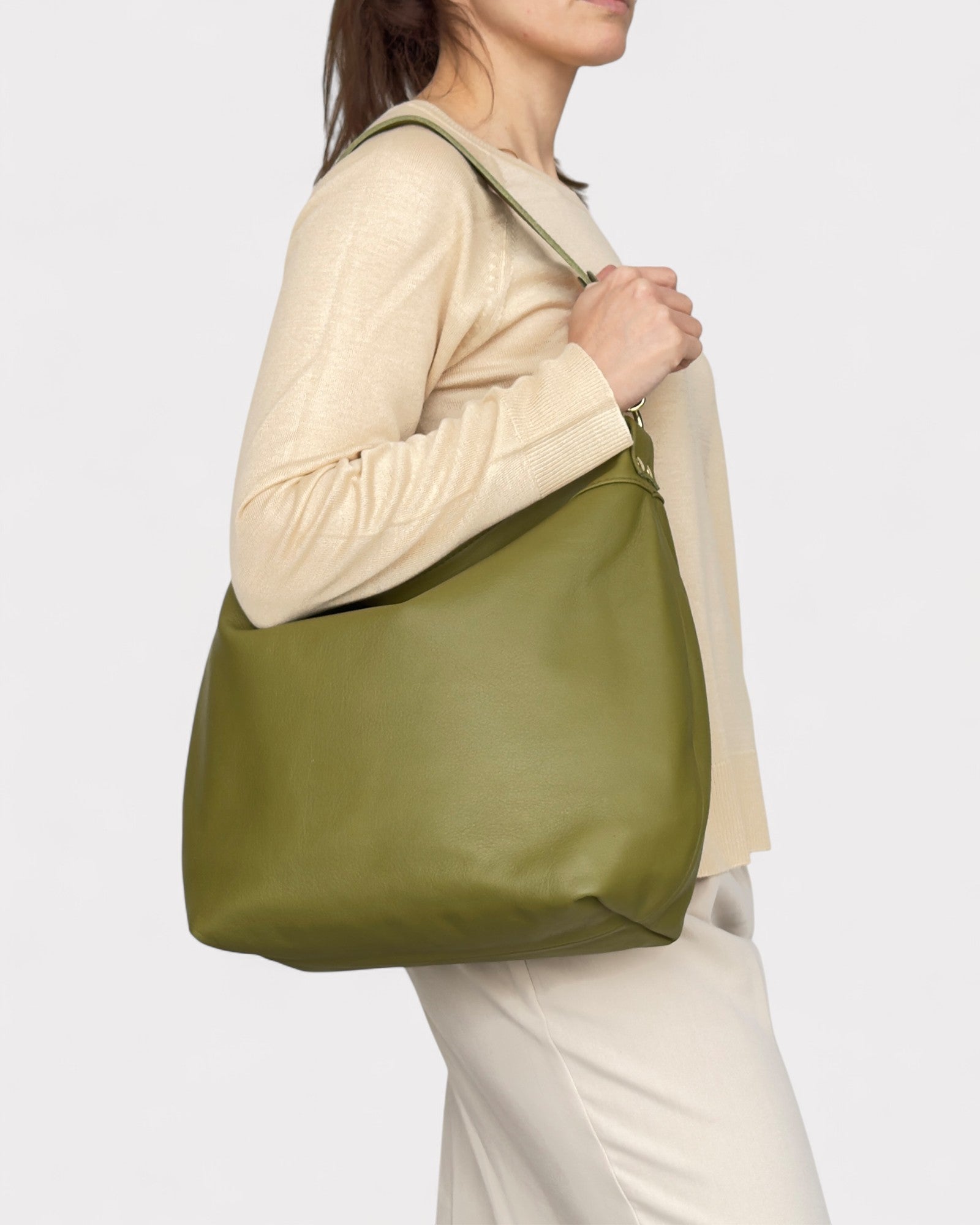 Person wearing a beige sweater and white pants with a green bag on a white background