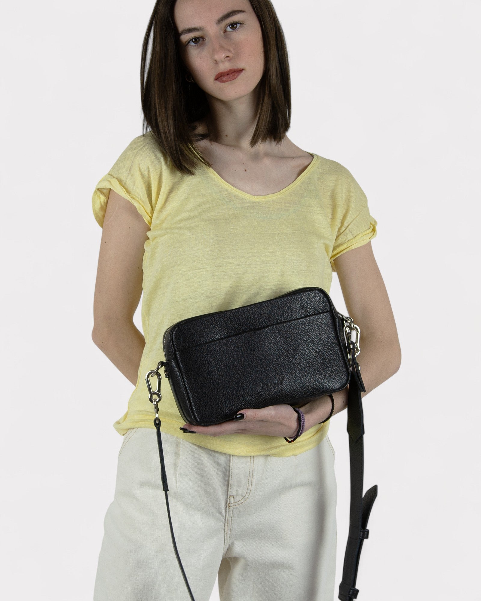 Woman holding a black leather crossbody bag against a white background