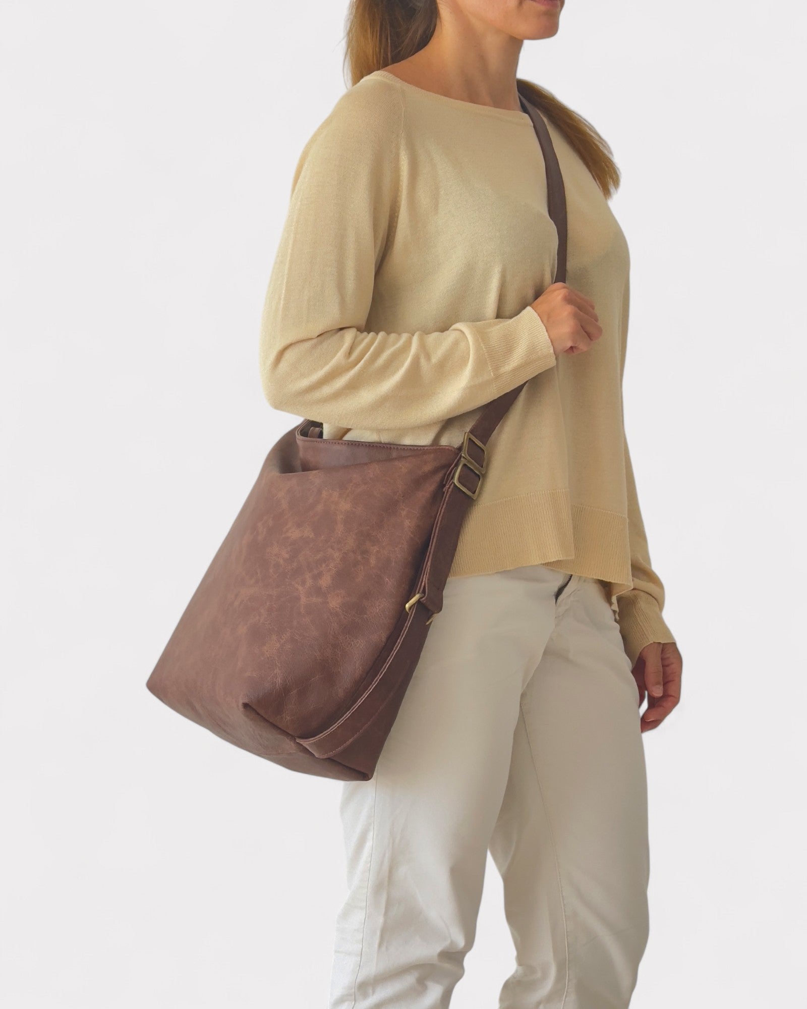 Woman carrying a brown leather hobo bag on a plain background