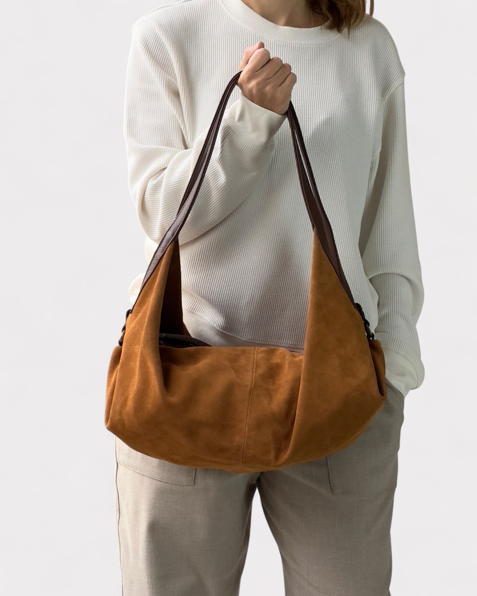 Person holding a tan leather bag against a white background