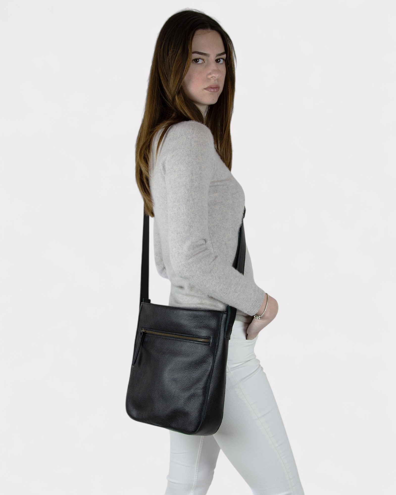 Woman carrying a black leather crossbody bag on a white background