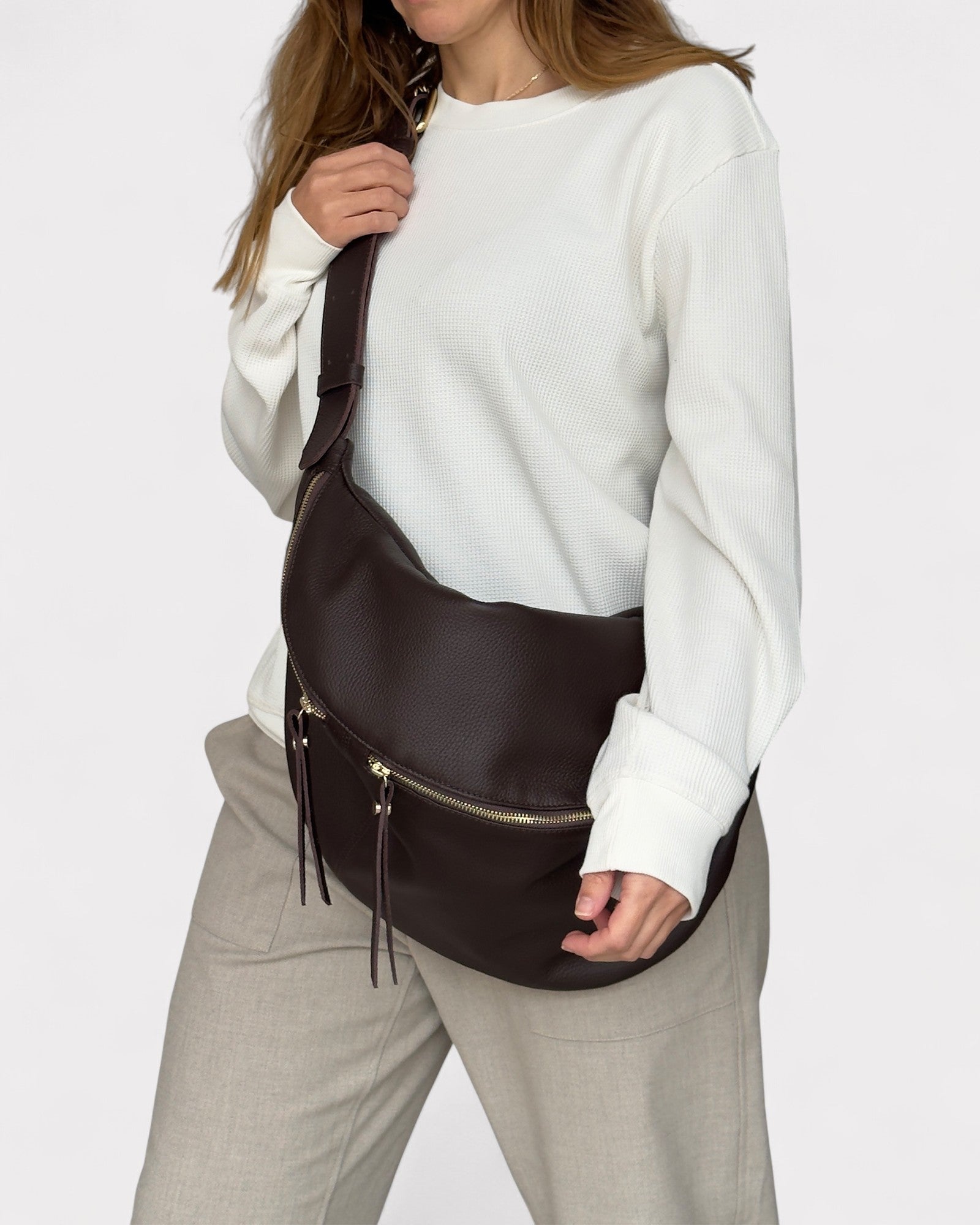 Person wearing a brown leather bag over one shoulder on a plain background