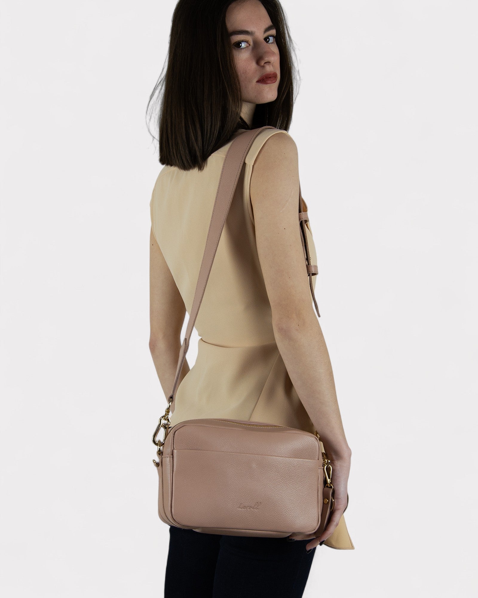 Woman wearing a dusty rose crossbody bag on a white background