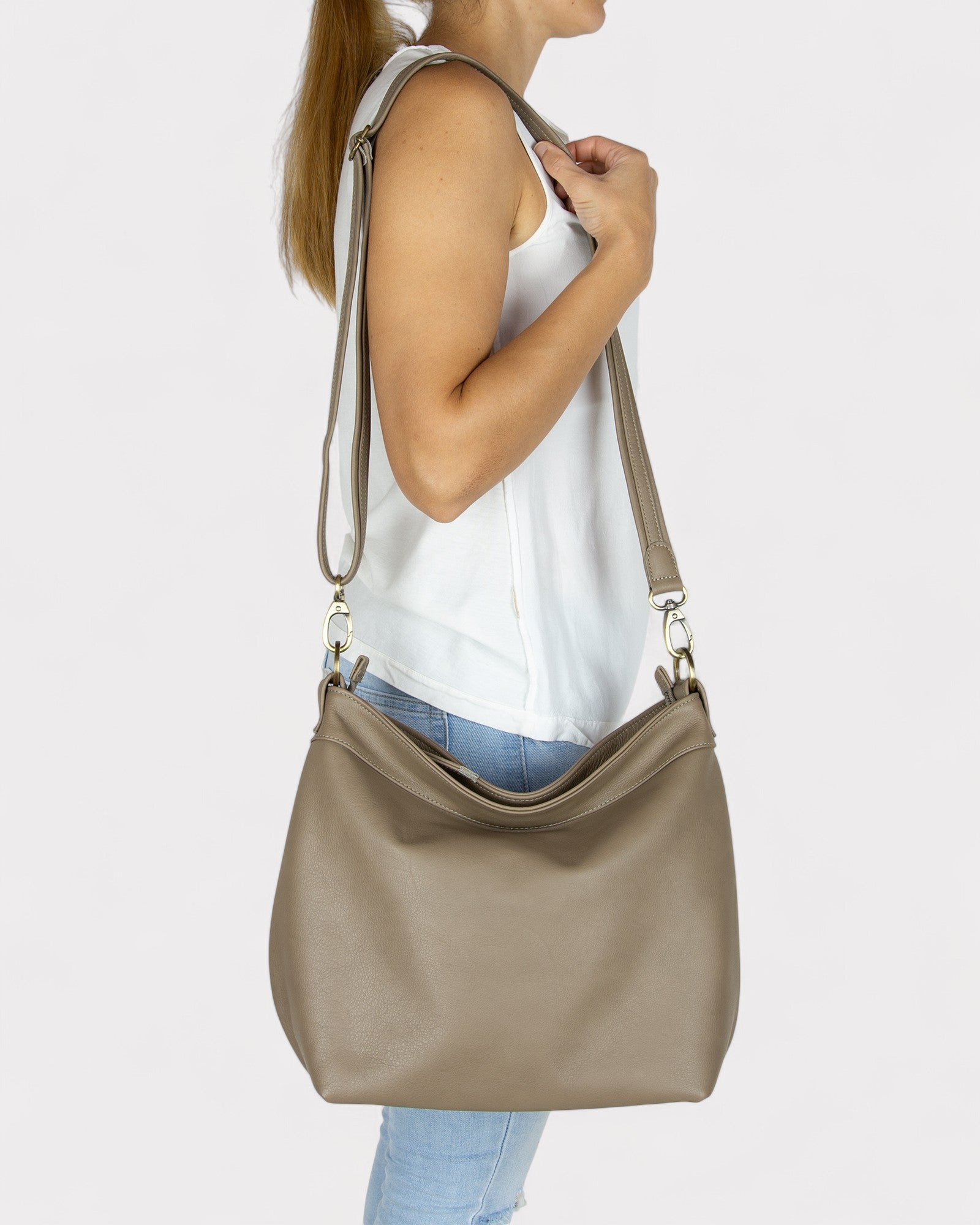 Person carrying a taupe handbag on a plain background