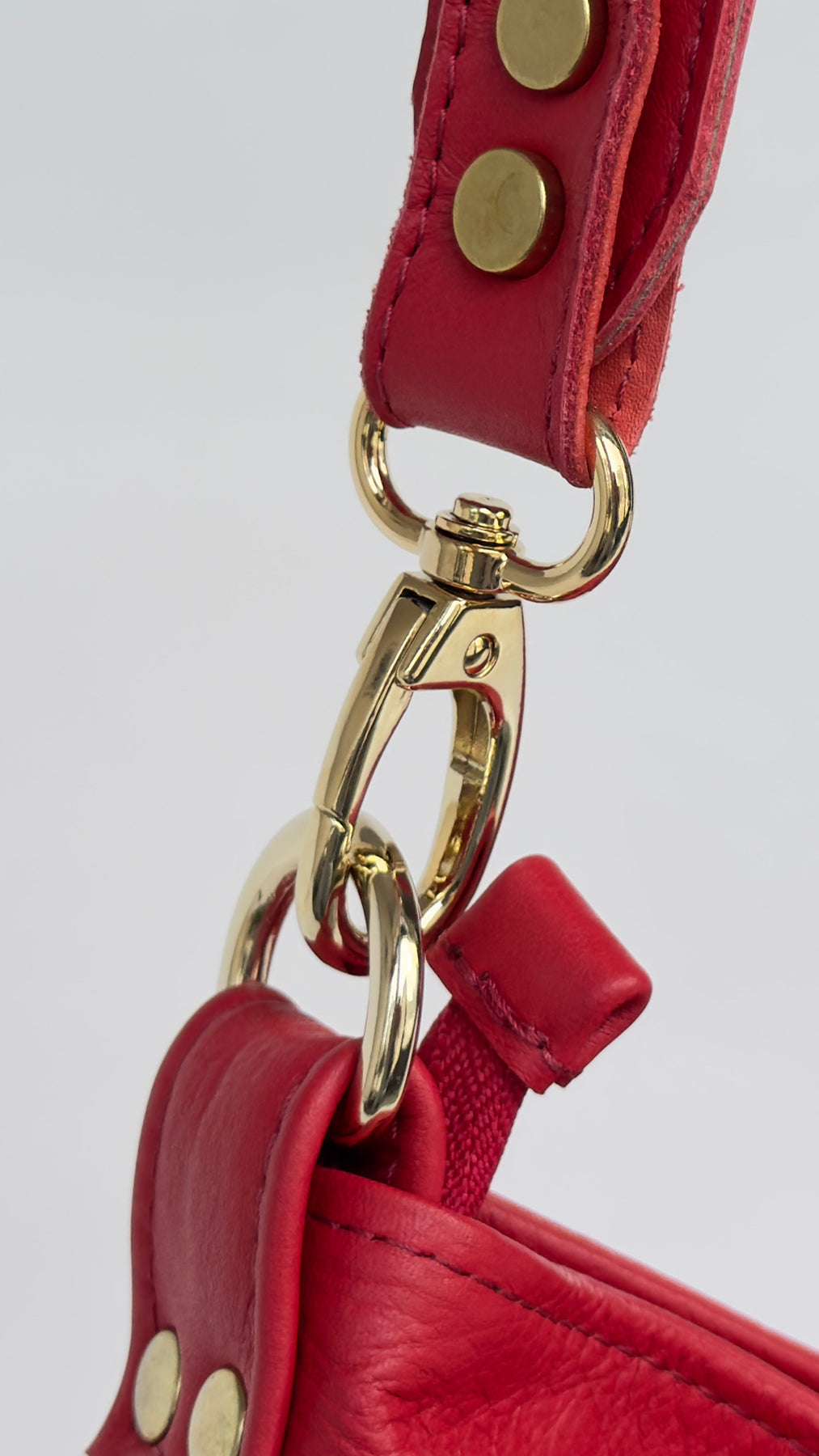 Close-up of a red leather strap with gold hardware on a light gray background