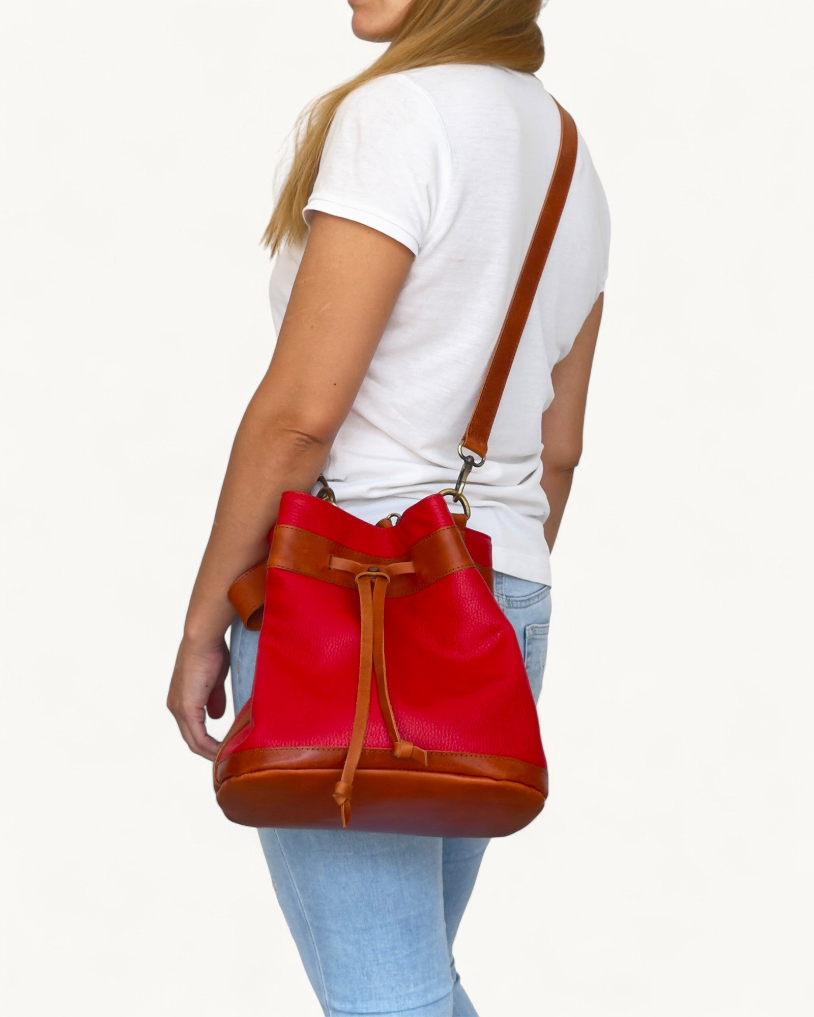 Red and brown leather bucket bag worn by a person on a white background