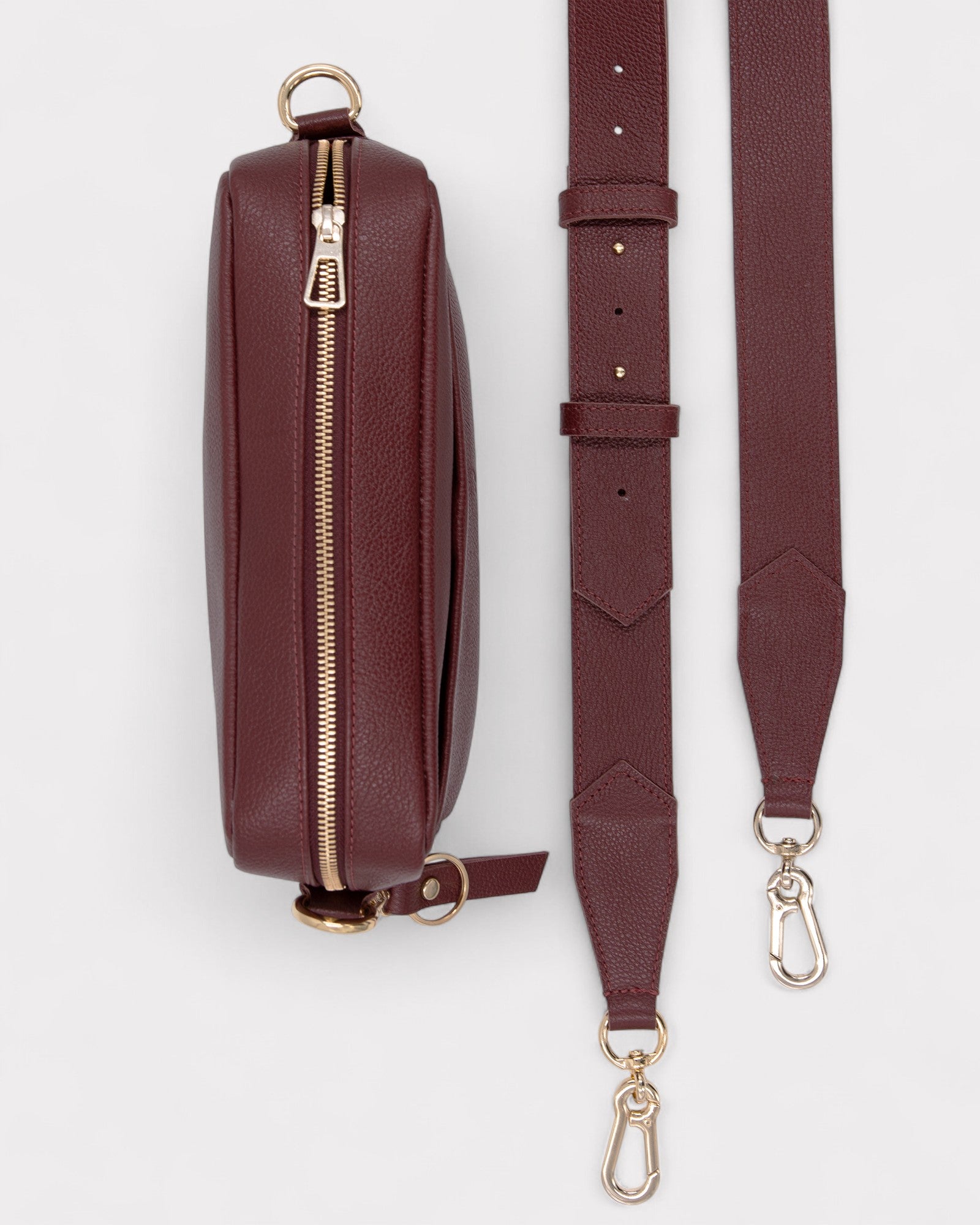 Burgundy leather bag with gold zipper and matching strap on a white background