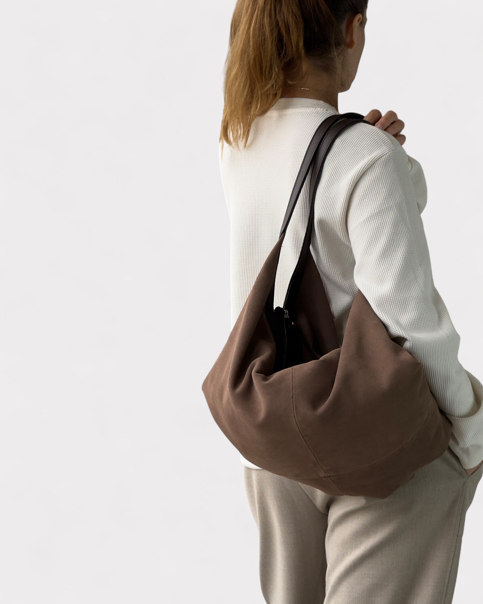 Person wearing a taupe shoulder bag on a plain background