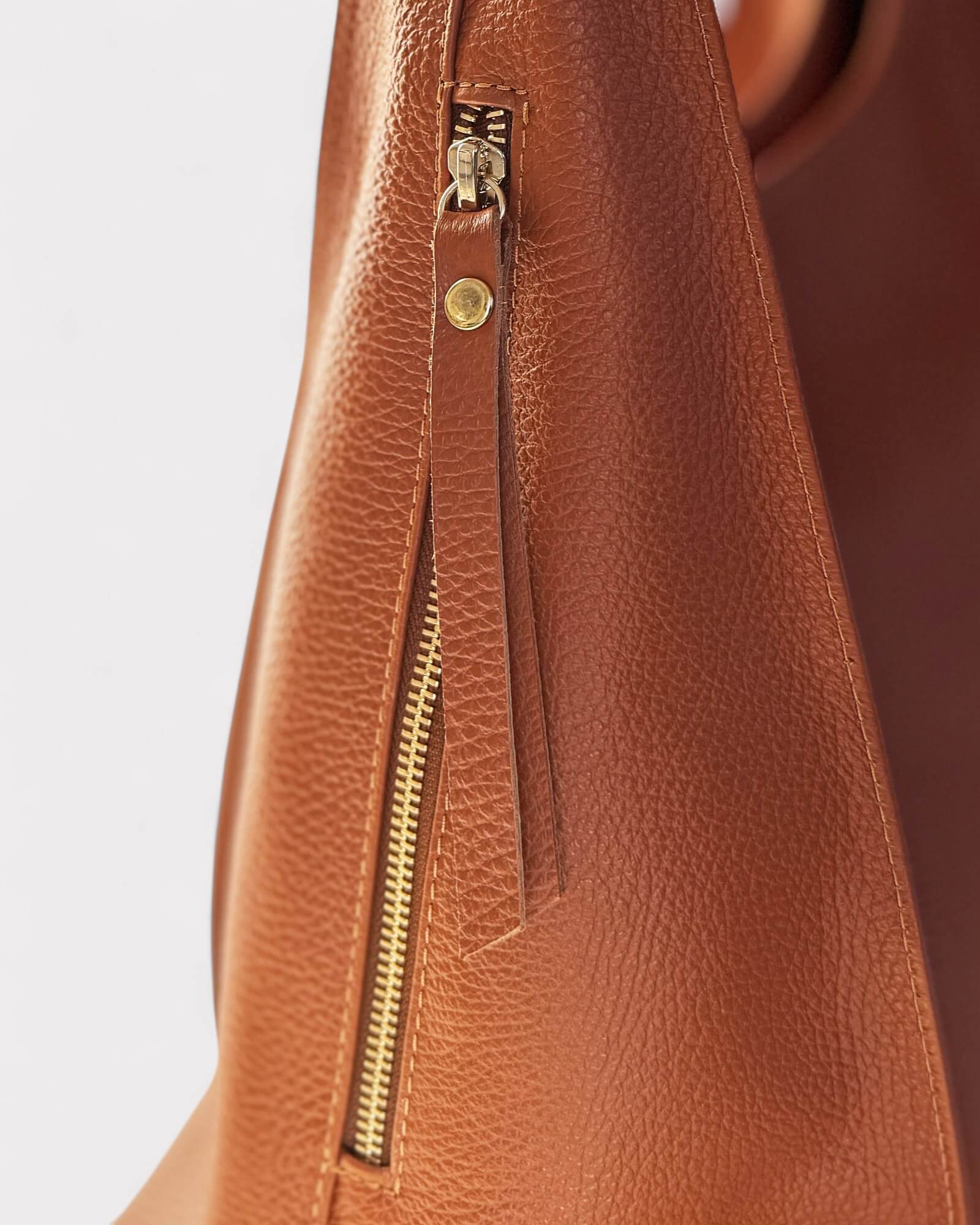 Close-up of a tan leather bag with a gold zipper and clasp.