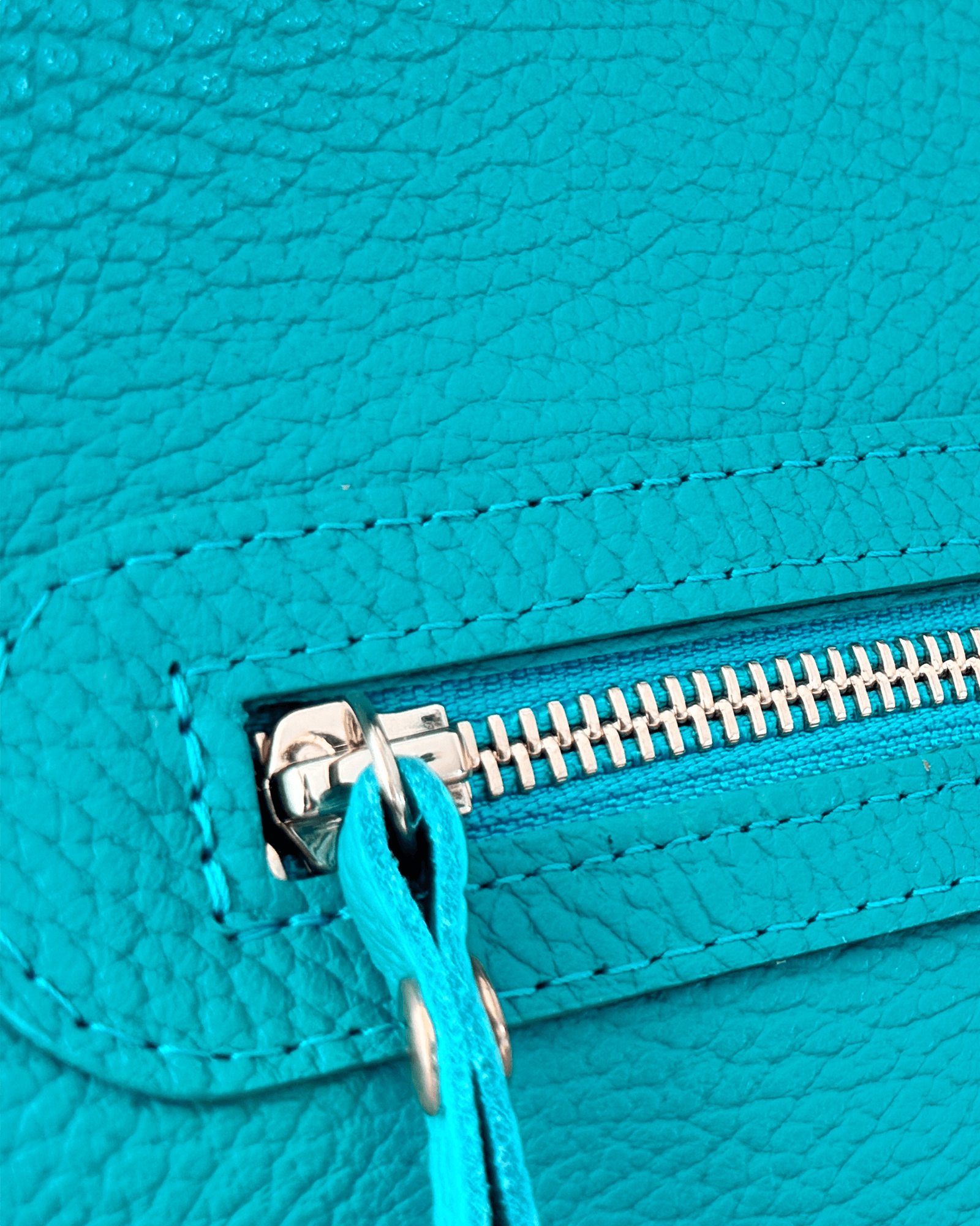 Close-up of a turquoise leather bag with a gold zipper.