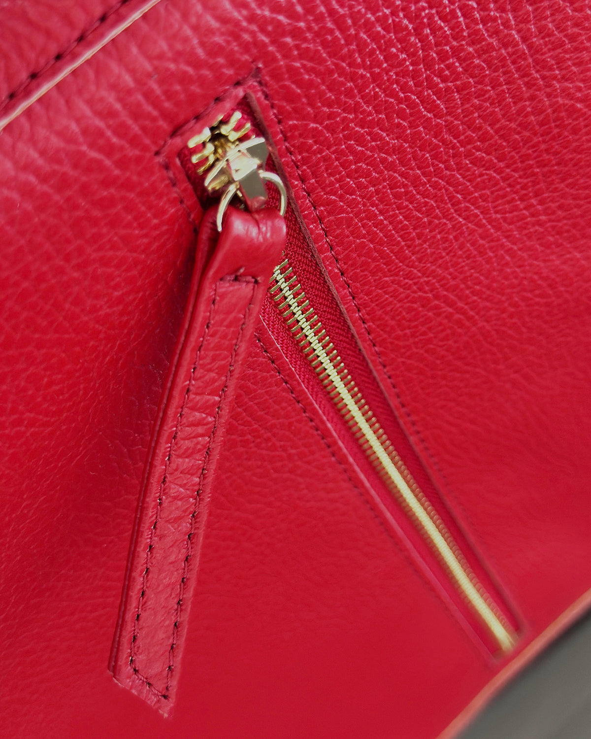 Close-up of a bright red pebbled leather bag with a gold-tone zipper and pull tab.